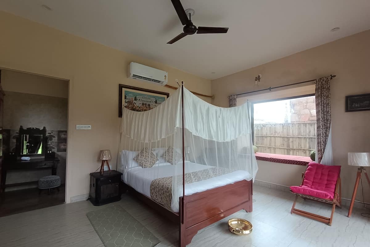 Ein Schlafzimmer mit Bett, Deckenventilator, Fenster mit Vorhängen, Nachttisch und kleinem Tisch mit Lampe.