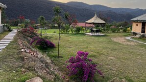 A rural landscape with a thatched-roof gazebo, a small building, and a stone pathway. - Chokhiwadi Forest Retreat (Thanagazi)