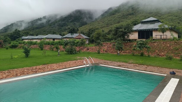 A swimming pool with a clear view of a mountainous landscape in the background. - Chokhiwadi Forest Retreat (Thanagazi)