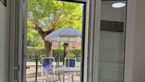 Une porte ouverte donnant sur un espace extérieur aménagé avec une table, des chaises et un parasol.