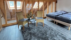A room with a high ceiling and wooden beams, featuring a sofa, two chairs, a small table with a plant, and skylights. - Gemütliches Ferienhaus für Große Familien und Gruppen (Kell am See)