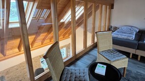 A high-ceilinged room with wooden beams, large windows, a sofa, and two wicker chairs. - Gemütliches Ferienhaus für Große Familien und Gruppen (Kell am See)