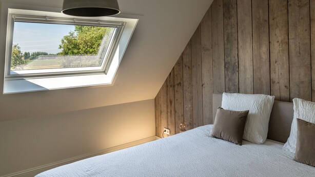 A bedroom with a skylight, a bed with pillows, and a wooden wall. - Heritage House 2 km From the Beach in Lissewege (Bruges)