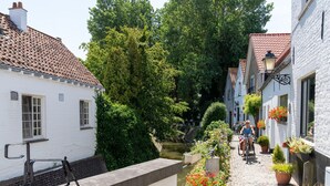 A narrow cobblestone street lined with white buildings, a bench, and potted plants. - Heritage House 2 km From the Beach in Lissewege (Bruges)