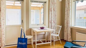 A room with a white table and chairs, a blue bag, and a window with curtains. - 2 Person Holiday Home in Ellos-by Traum (Ellos)
