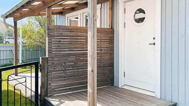 A wooden deck with a metal railing, a white door with a circular window, and a wooden fence. - 2 Person Holiday Home in Ellos-by Traum (Ellos)