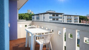 Un balcon avec une table et des chaises blanches, un ciel bleu dégagé et des bâtiments en arrière-plan.