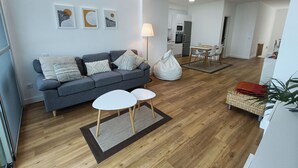 A modern living room with a grey sofa, two small tables, and a dining area with a white table and chairs.