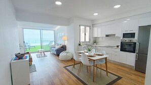 A modern kitchen with white cabinets, a dining area with a table and chairs, and a view of the sea through a large sliding glass door.