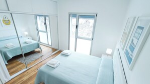 A modern bedroom with a large bed, a smaller bed, a mirror, and a window.