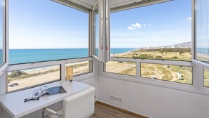 Una habitación con escritorio y ventanas amplias con vista a la playa y un paisaje lejano.