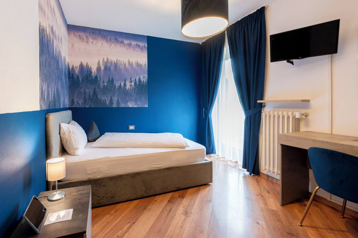 A modern bedroom with a bed, bedside table, lamp, and a mounted TV.