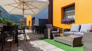 An outdoor seating area with wicker furniture, a white umbrella, and a view of mountains. - Kyrr Smart Mountain Retreat (Moena)