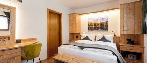 A modern bedroom with a wooden bed, a desk, a chair, and a painting of a mountain landscape.