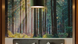 Ein Schlafzimmer mit großem Wandbild zum Thema Wald, einem Doppelbett mit weißer und schwarzer Bettwäsche sowie einer modernen Pendelleuchte.