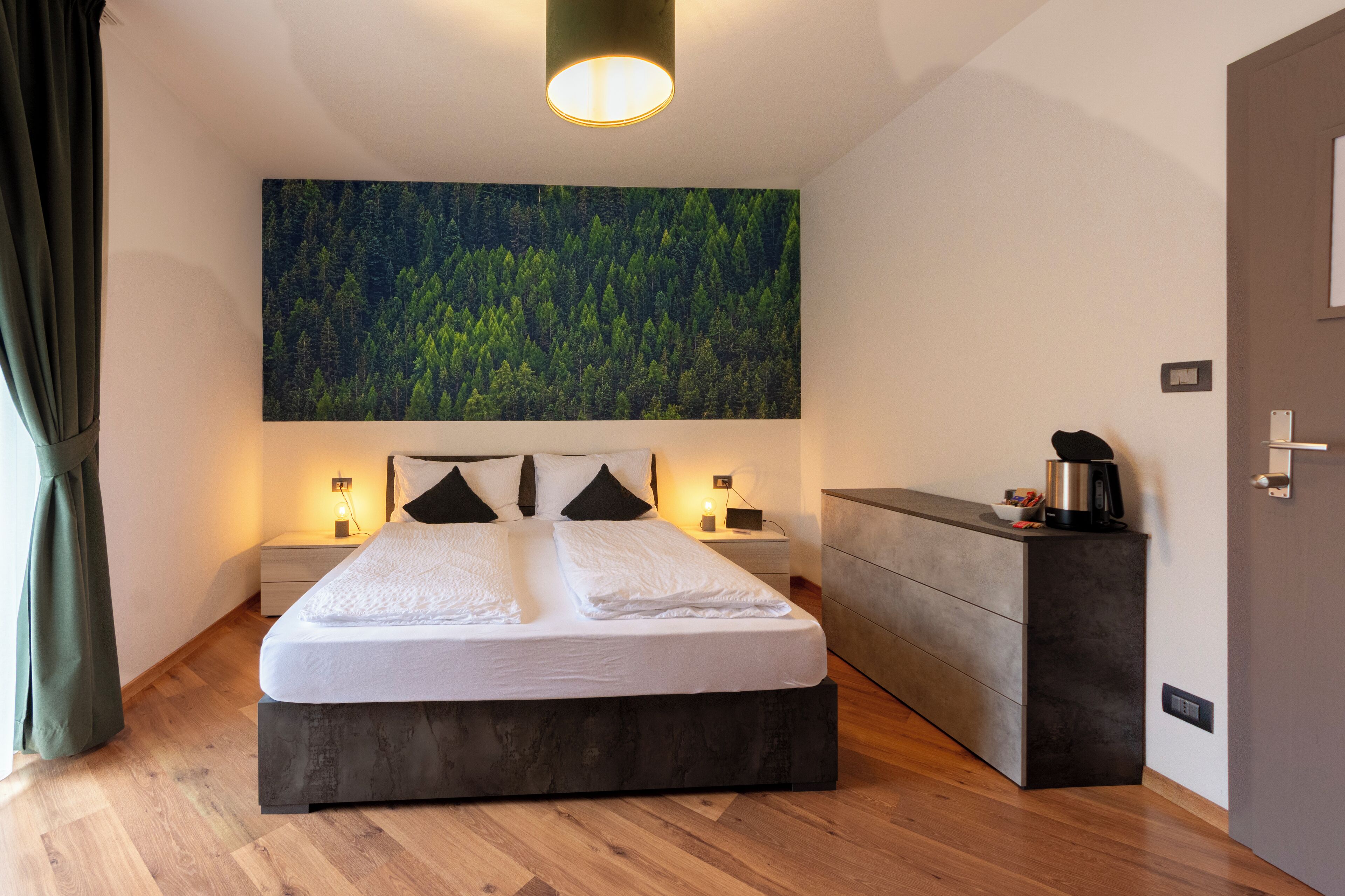 A modern bedroom with a large bed, bedside tables, a built-in bench, and a large forest-themed wall mural.