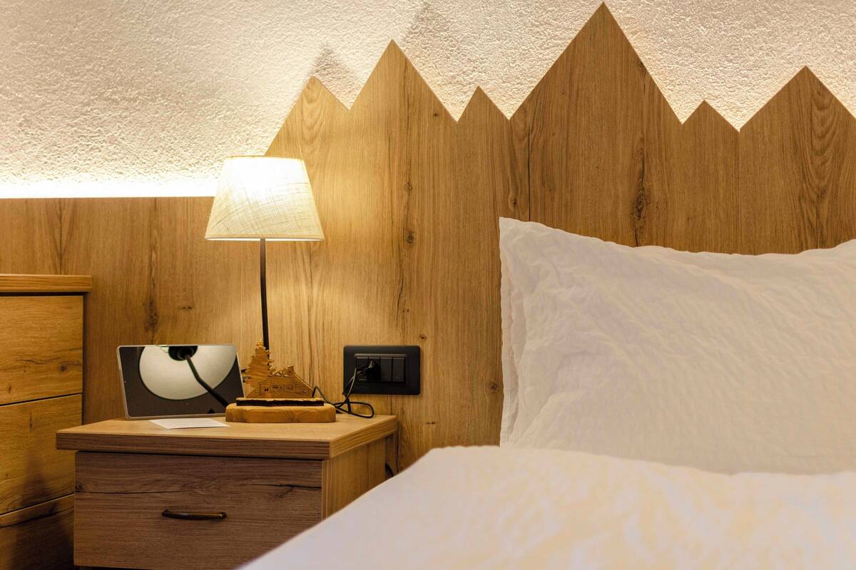 A wooden headboard with a unique zigzag pattern, a bedside lamp, a wooden nightstand with a lamp, and a bed with white bedding.