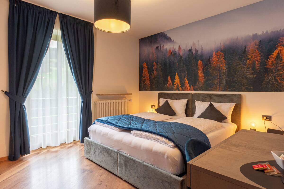 A bedroom with a bed, a nightstand, a lamp, and a painting of a forest.