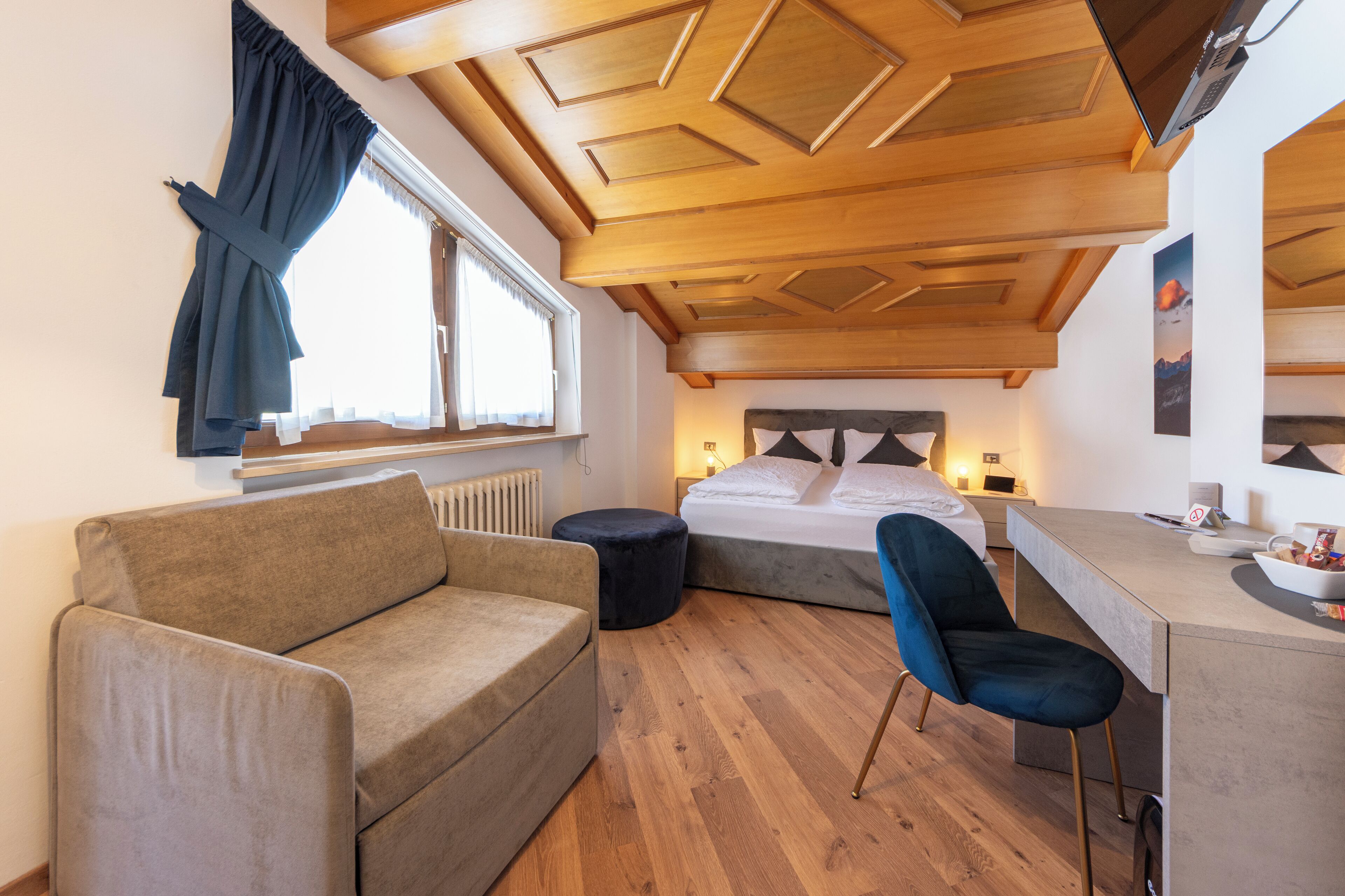 Una habitación moderna con techo de madera, una cama, un sofá, un escritorio y una silla.