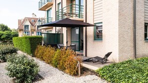A multi-story residential building with a balcony, outdoor seating area, and a gravel pathway. - Artemis Gvo2 Apartment in Koksijde Near the Beach (Koksijde)