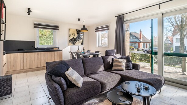 A modern living room with a sectional sofa, a dining area, and a kitchen. - Artemis Gvo2 Apartment in Koksijde Near the Beach (Koksijde)