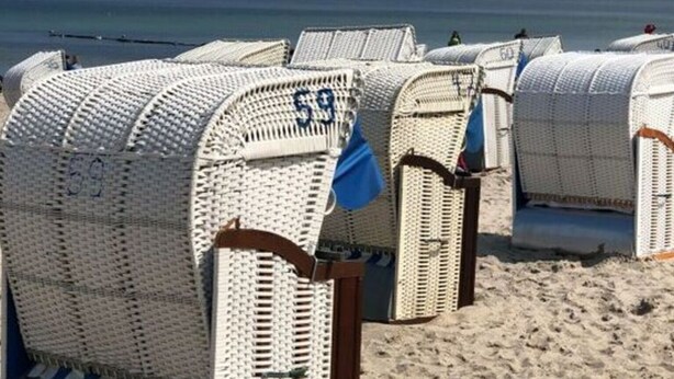 Beach chairs with numbers on them, arranged on a sandy beach with the ocean and a sailboat in the background. - Juchmann Modern Retreat (Timmendorfer Strand)