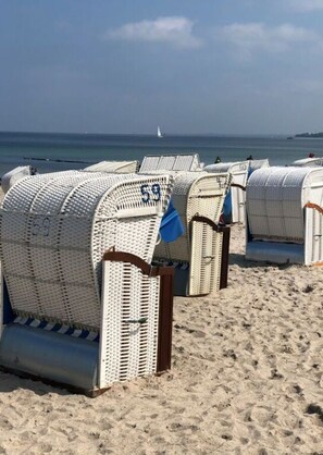 Beach chairs with numbers on them, arranged on a sandy beach with the ocean and a sailboat in the background. - Juchmann Modern Retreat (Timmendorfer Strand)