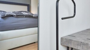A modern bedroom with a bed, a nightstand, and a wall-mounted black metal handle. - Juchmann Modern Retreat (Timmendorfer Strand)