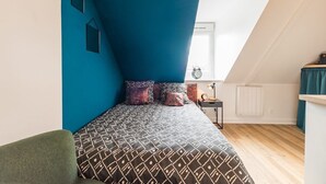 A bedroom with a sloped ceiling, a bed with patterned bedding, a nightstand, and a window with a view. - Central and charming studio, Guingamp center (Guingamp)