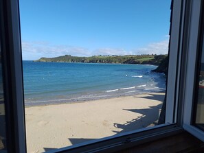 Une vue sur la plage à travers une fenêtre, avec une eau d’un bleu limpide et une plage de sable.