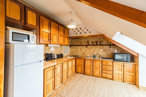 Une cuisine avec des meubles de rangement en bois, un réfrigérateur blanc, un four à micro-ondes, un grille-pain et un autre four à micro-ondes noir posé sur le plan de travail.