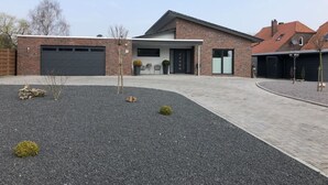 Una casa moderna de dos pisos con fachada de ladrillo, garaje y entrada con grava y pequeños arbustos.