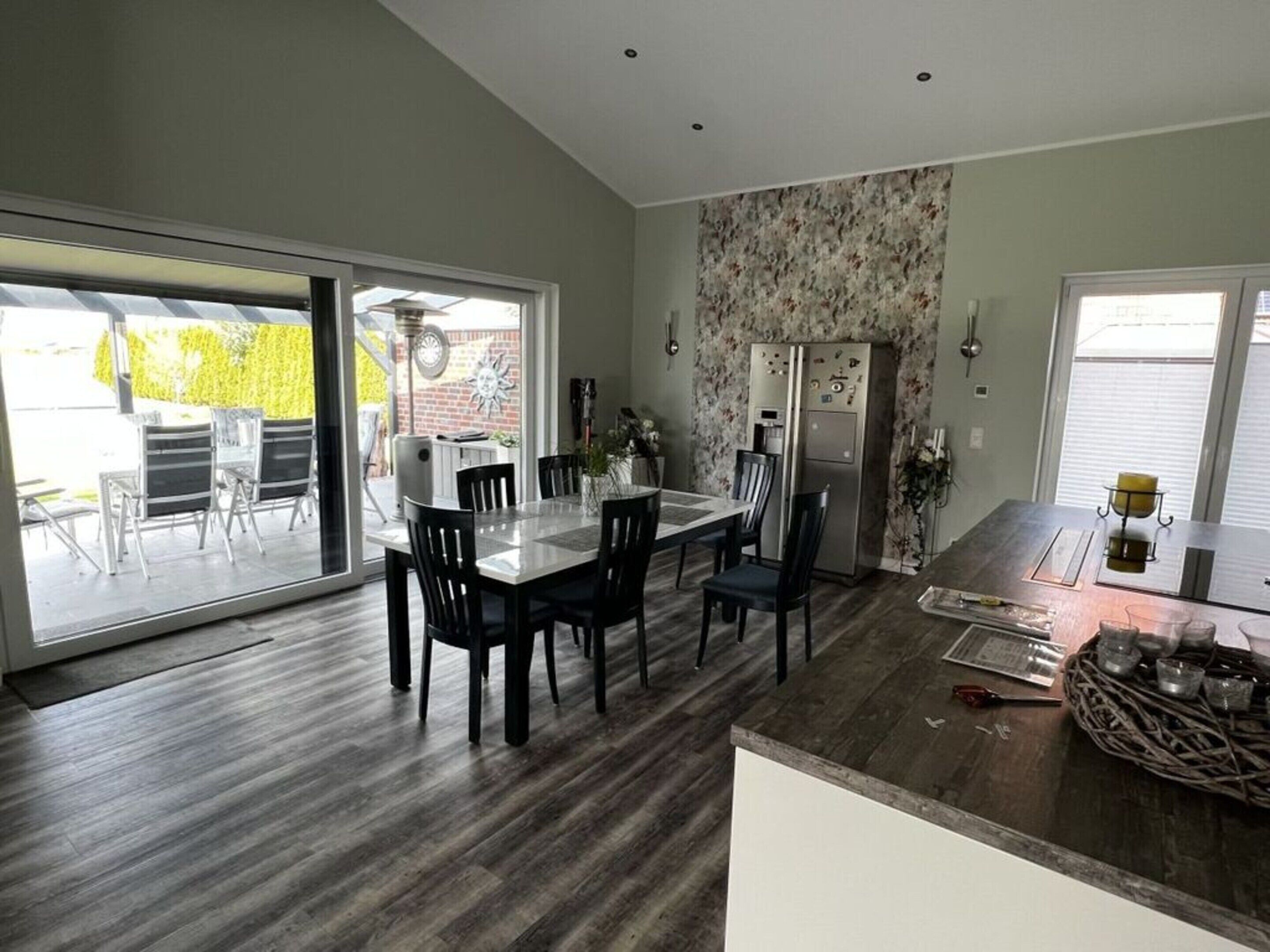 A modern kitchen with a dining area, large windows, and a sliding glass door leading to an outdoor patio.