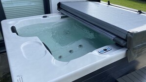 Un jacuzzi con panel de control, un banco y una terraza de madera.