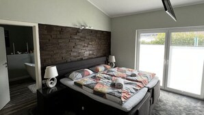 Un dormitorio moderno con un cabecero de diseño ladrillo, una cama grande con colcha colorida, dos lámparas de noche y un ventanal corredero que da a un balcón.