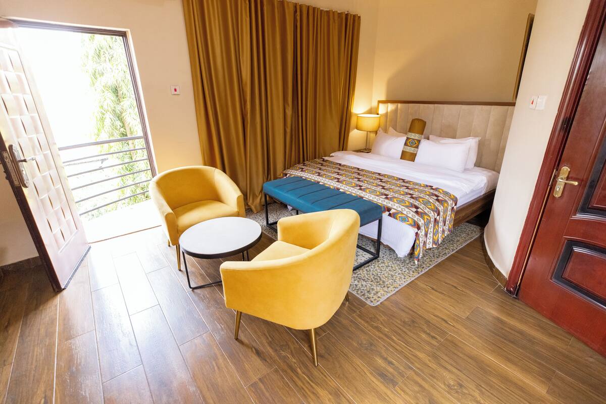 A hotel room with a bed, two chairs, a small table, and a window with curtains.