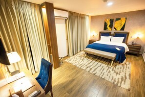 A hotel room with a bed, a desk with a lamp, a chair, and a large window with curtains. - Volta Serene Hotel (Ho)