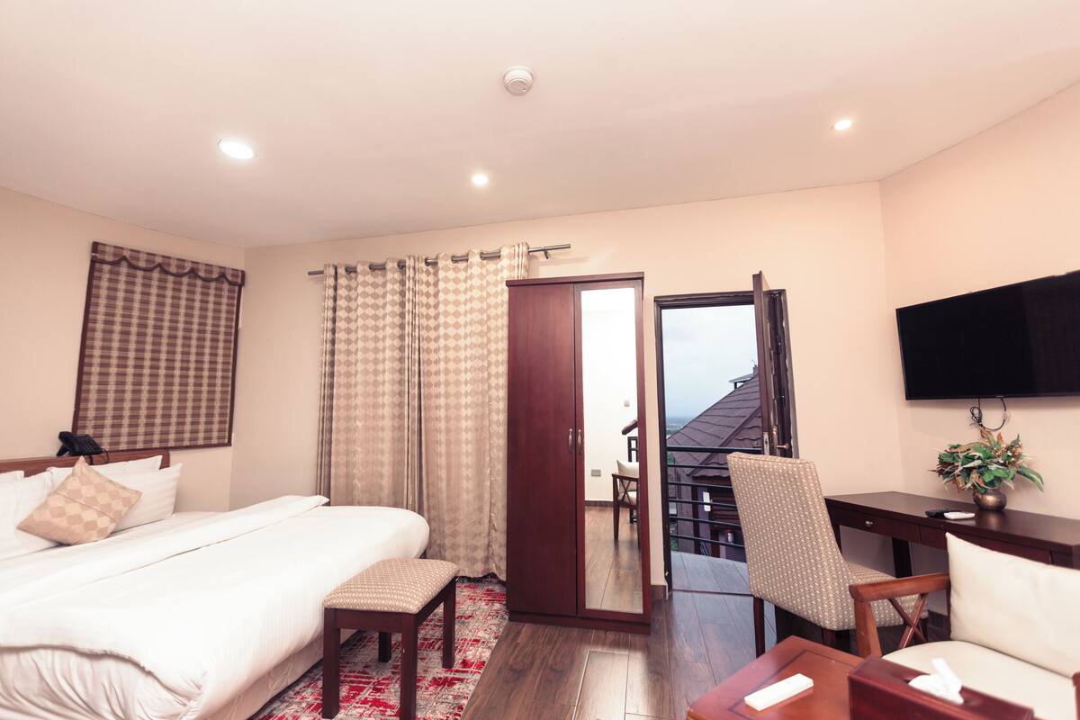 A hotel room with a bed, a desk, a chair, a TV, and a balcony with a view.