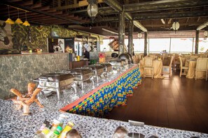 A restaurant with a long buffet table, a counter with a cash register, and a wooden ceiling. - Volta Serene Hotel (Ho)