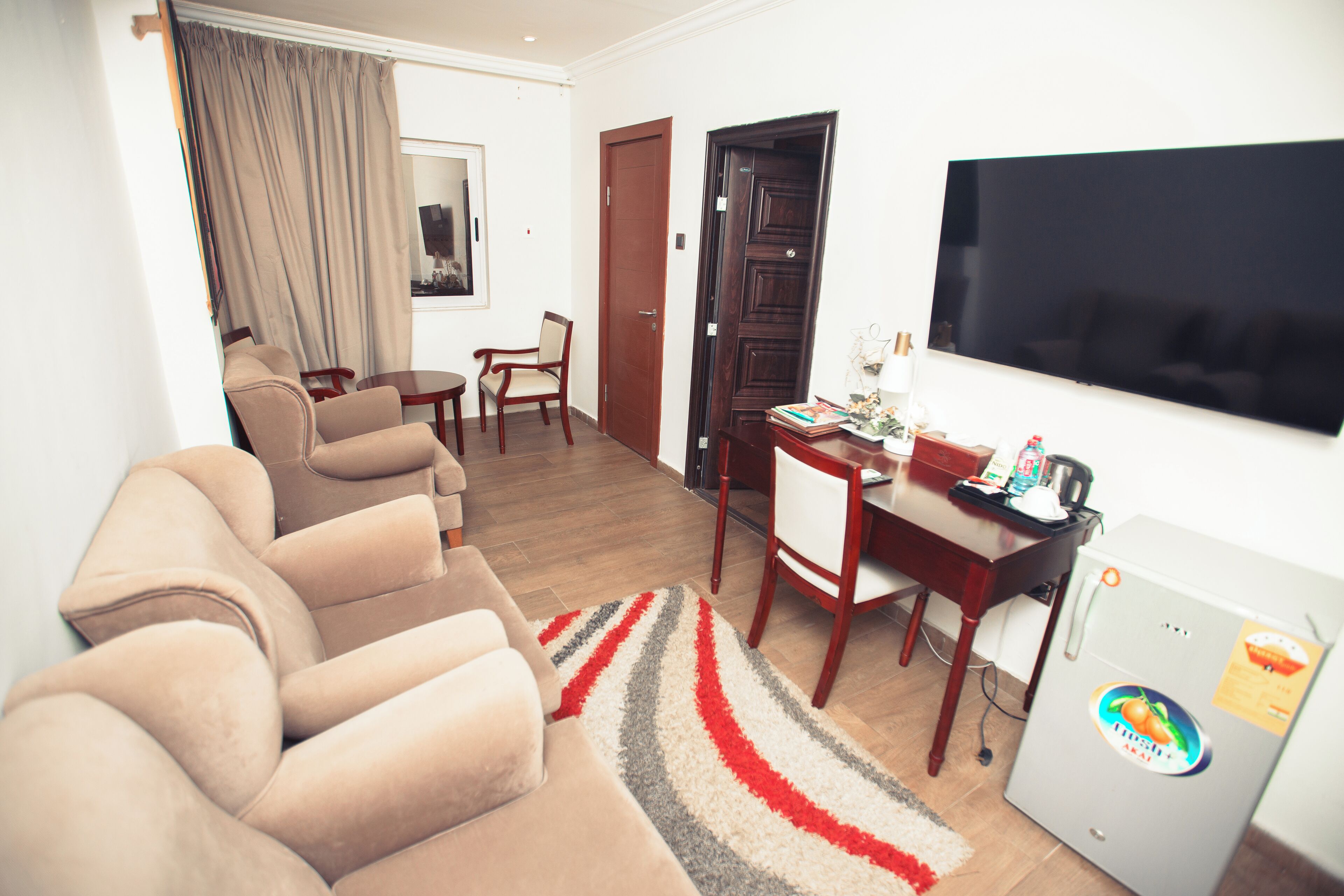A living room with a sofa set, a dining table, chairs, a TV, and a refrigerator.