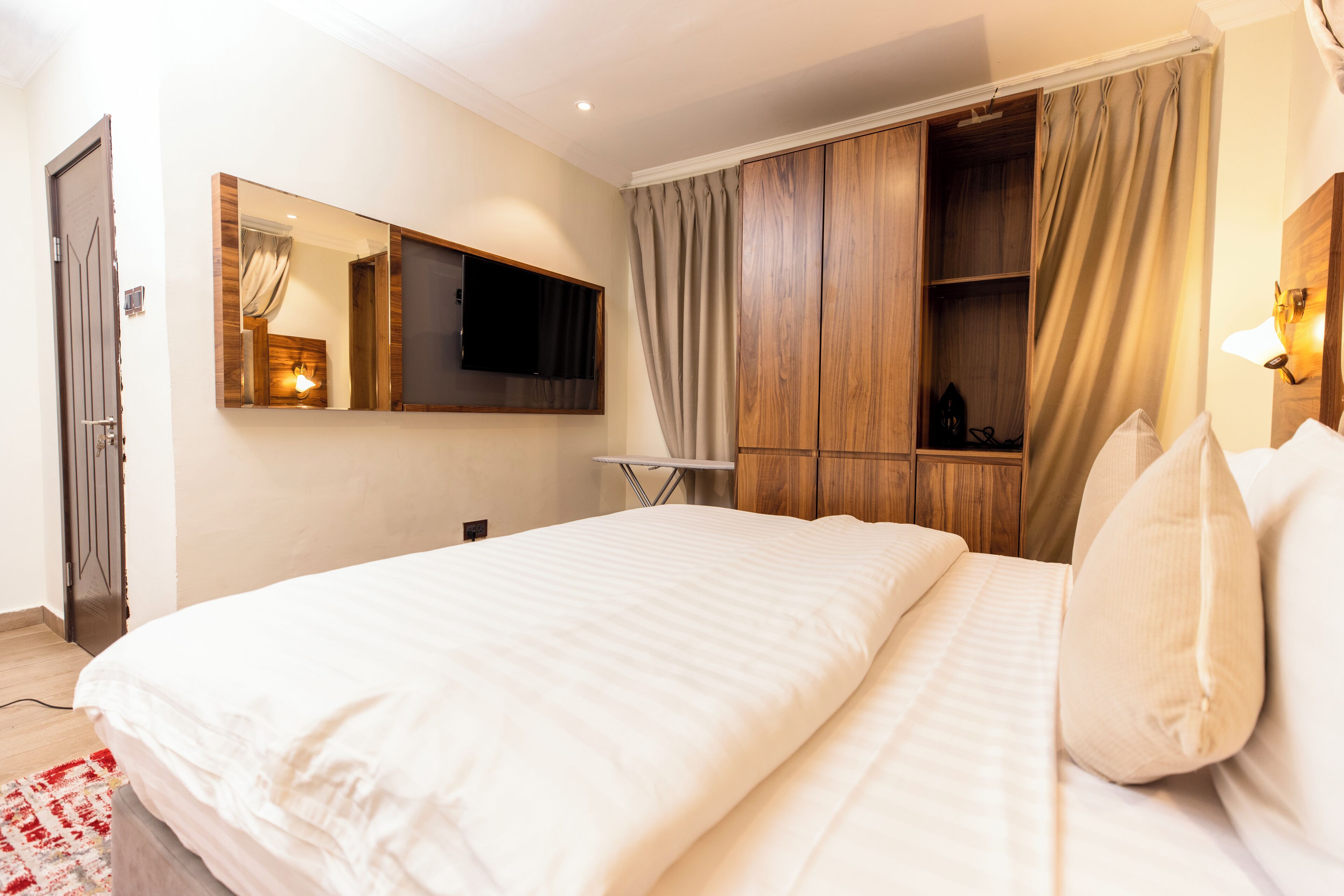 A bedroom with a large bed, a TV mounted on the wall, and a wardrobe.