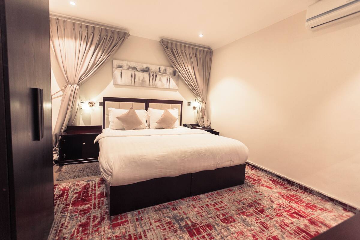 A neatly arranged bedroom with a large bed, two bedside tables, and a headboard with a light fixture.