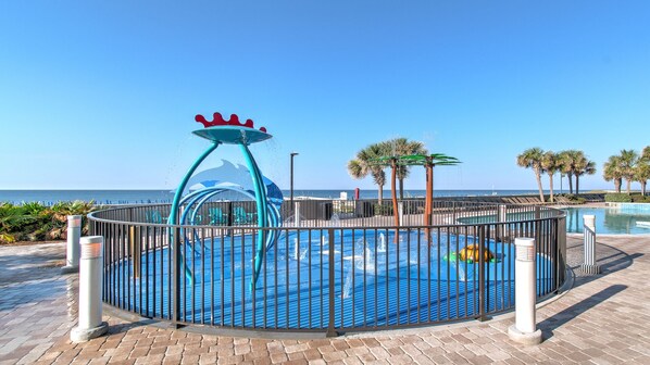 A water park with a circular pool, a water slide with a crown-shaped top, and palm trees in the background. - Beachfront! Lazy River, Restaurant, New condo! (Orange Beach)