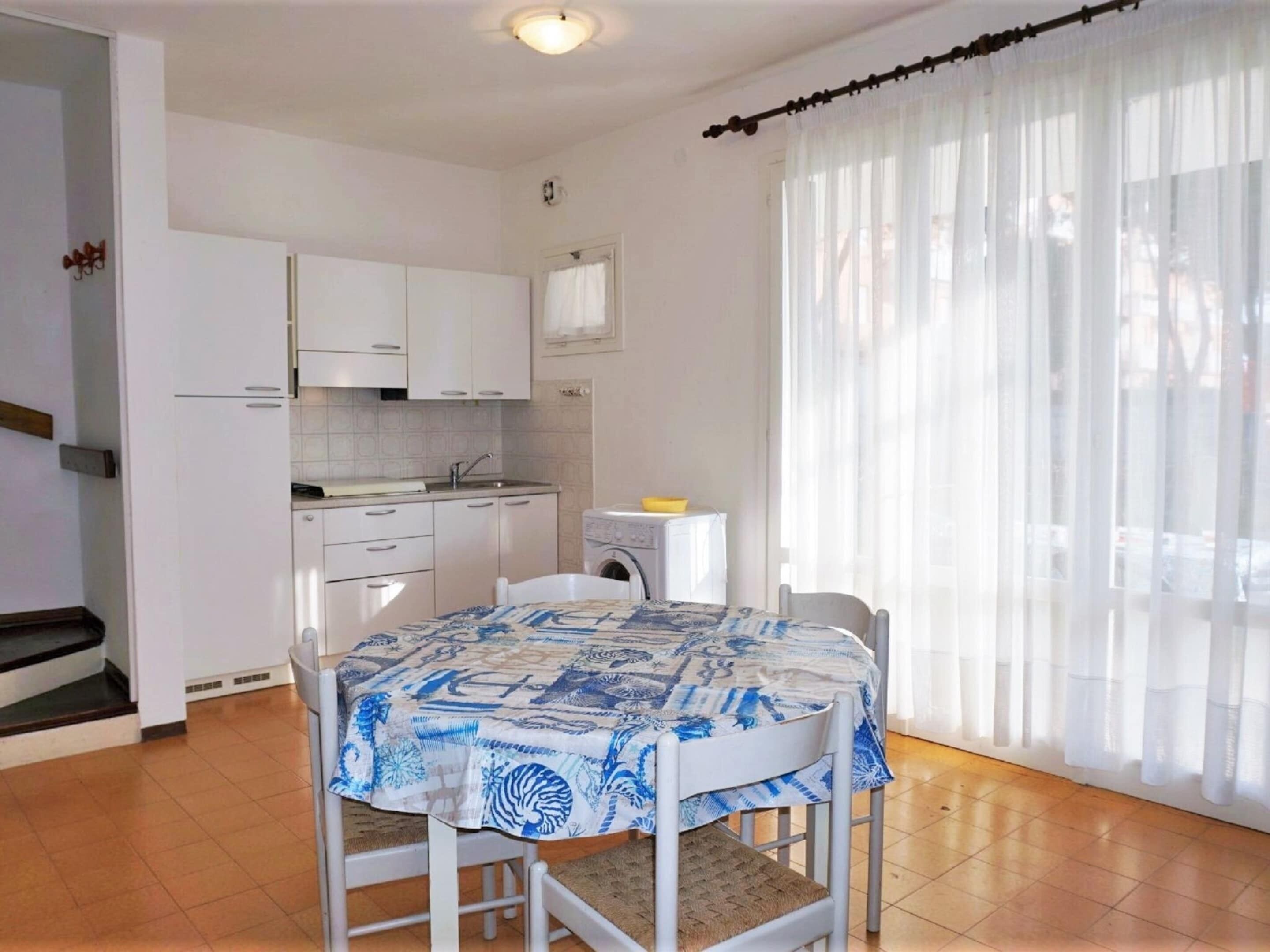 A small kitchen with white cabinets, a sink, and a washing machine. There is a table with a blue and white patterned tablecloth.
