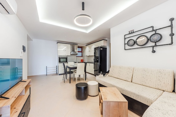 A modern living room with a flat-screen TV, a wooden coffee table, a sofa, and a dining area with chairs.