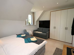 Ein modernes Schlafzimmer mit einem großen Bett, einem grauen Sofa, einem Kleiderschrank und einem Fenster mit Blick.