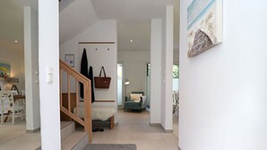 A spacious hallway with a wooden staircase leading to a bedroom. A grey rug is on the floor, and a brown handbag hangs on the wall. - Villa Ostseekind Comfortable Holiday Residence (Ostseebad Dierhagen)