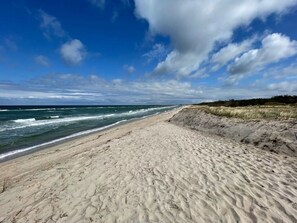 A sandy beach with waves, a clear sky, and a distant tree line. - Villa Ostseekind Comfortable Holiday Residence (Ostseebad Dierhagen)