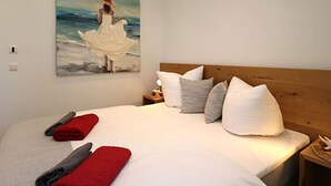 A bedroom with a large bed, pillows, a nightstand, and a painting of a woman by the sea. - Villa Ostseekind Comfortable Holiday Residence (Ostseebad Dierhagen)