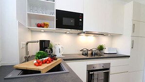 A modern kitchen with white cabinets, a black microwave, a coffee maker, and a cutting board with tomatoes. - Villa Ostseekind Comfortable Holiday Residence (Ostseebad Dierhagen)